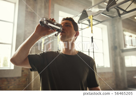 Refreshing. Young athletic man drinking fresh water from the bottle while exercising at gym Refreshing. Young athletic man drinking fresh water from the bottle while exercising at gym 56465205