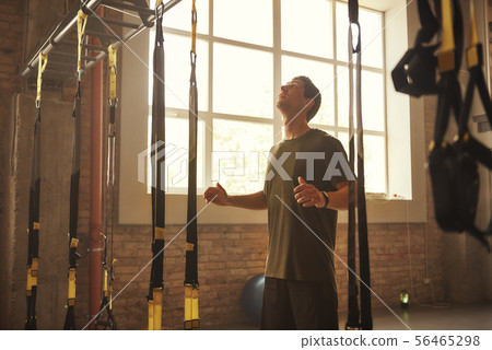 Ready to do my best Strong athletic man looking at trx fitness straps while standing at gym 56465298