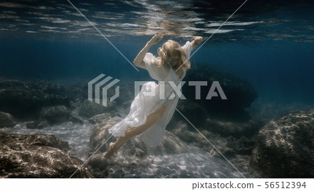 Woman in white swims underwater in the sea 56512394