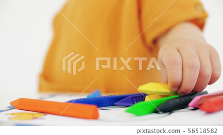 Blonde baby girl putting yellow crayon on the table 56518582