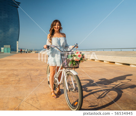 Asian model in a blue dress rides a white bicycle in a green park Asian model in a blue dress rides a white bicycle in a green park 56534945