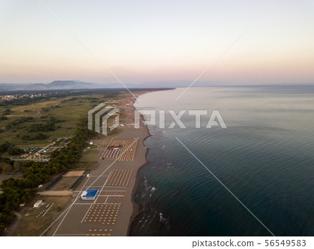 Aerial view of sandy beach with yellow sunbeds and wooden umbrellas at sunset Aerial view of sandy beach with yellow sunbeds and wooden umbrellas at sunset 56549583