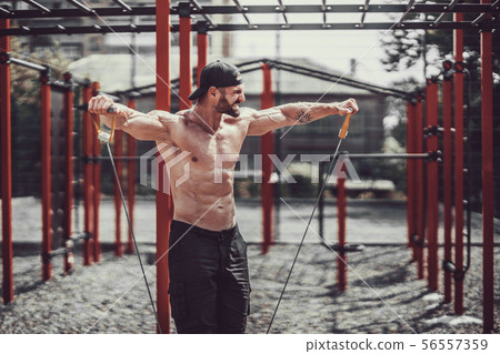 Fitness man exercising with stretching band in outdoor gym. 56557359