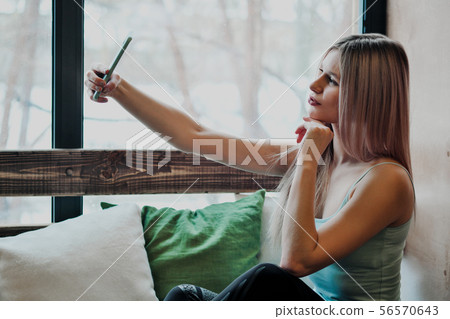 Young beautiful athletic woman blonde in sportswear sitting by the window of a cafe and using a Young beautiful athletic woman blonde in sportswear sitting by the window of a cafe and using a 56570643