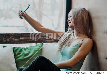 Young beautiful athletic woman blonde in sportswear sitting by the window of a cafe and using a Young beautiful athletic woman blonde in sportswear sitting by the window of a cafe and using a 56570644