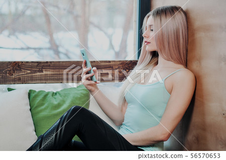 Young beautiful athletic woman blonde in sportswear sitting by the window of a cafe and using a Young beautiful athletic woman blonde in sportswear sitting by the window of a cafe and using a 56570653
