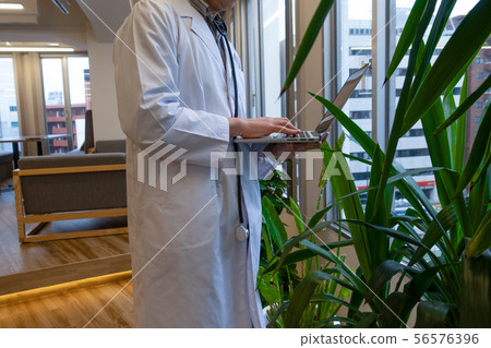 A doctor in a white coat who operates a laptop on the palm of his hand A doctor in a white coat who operates a laptop on the palm of his hand 56576396