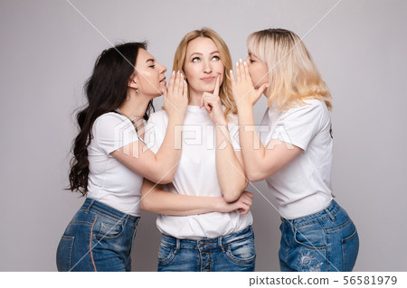 Gossiping girls whispering a secret to their Gossiping girls whispering a secret to their 56581979