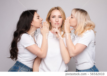 Gossiping girls whispering a secret to their Gossiping girls whispering a secret to their 56582010