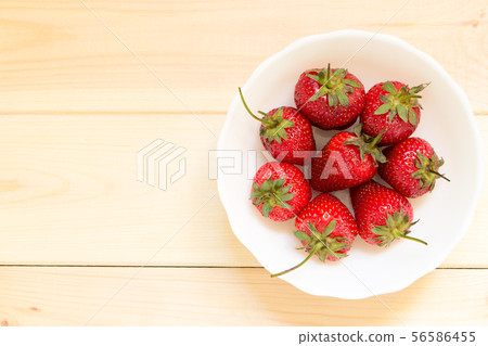 Red ripened strawberries in white bowl on wooden table with copy space. 56586455