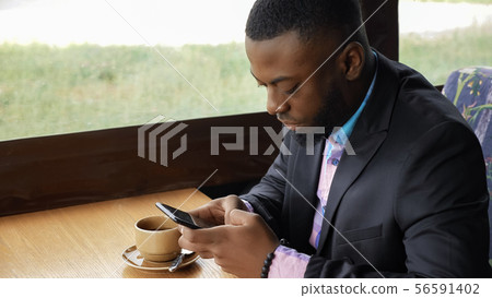 Afro american businessman is typing a message on smartphone sitting in cafe. Afro american businessman is typing a message on smartphone sitting in cafe. 56591402