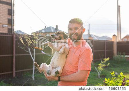 People, pets and dogs concept - young man hugging funny Jack Russell Terrier outdoors 56605263