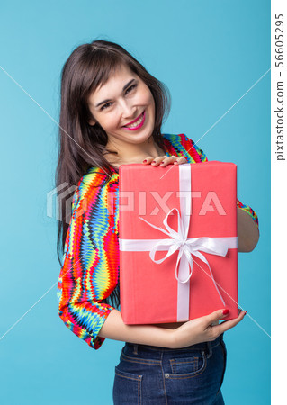 Cheerful good looking young brunette woman holding a red gift box in her hands, but against a blue 56605295