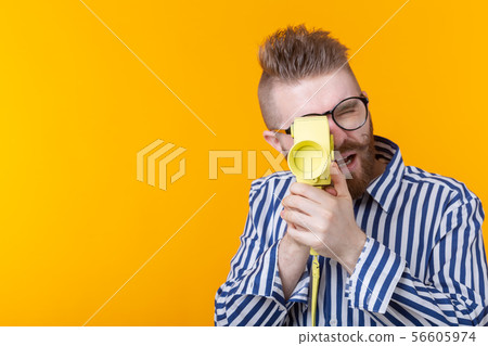 Unidentified young man with a yellow camera with a mustache and a beard on a yellow background 56605974