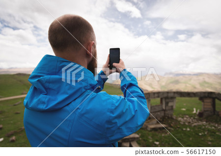 A bearded man takes photos or videos outdoors on his smartphone. A guy in a jacket on a background A bearded man takes photos or videos outdoors on his smartphone. A guy in a jacket on a background 56617150