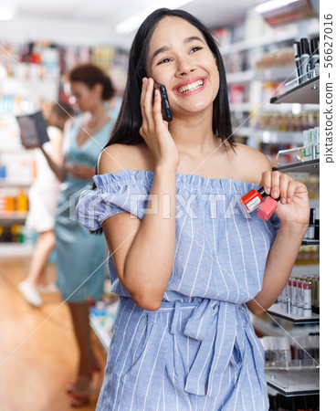Stylish woman with nail polish talking by phone in store Stylish woman with nail polish talking by phone in store 56627016