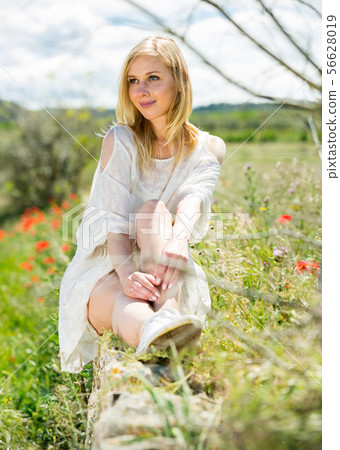 Woman wearing white dress posing near fields with wild flowers 56628019