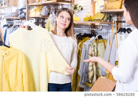 Asistant demonstration fashion yellow pullover to woman in boutique 56628280