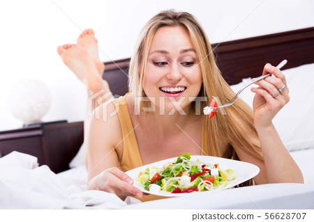 Woman lying in the bed and eating salad Woman lying in the bed and eating salad 56628707