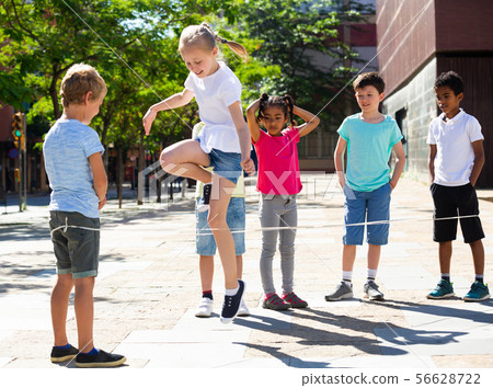 Energetic kids playing and skipping on elastic jumping rope in european yard 56628722