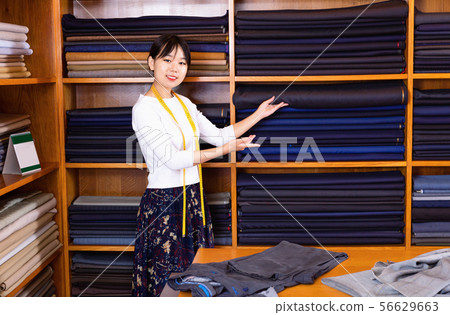 Chinese young female seller of fabric shop showing new trendy textiles of high quality for dressmaking Chinese young female seller of fabric shop showing new trendy textiles of high quality for dressmaking 56629663