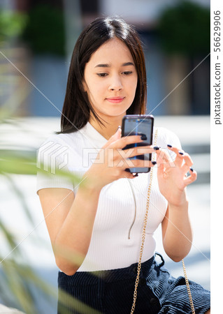 Portrait of smiling young girl teenager messaging on phone outdoors Portrait of smiling young girl teenager messaging on phone outdoors 56629906