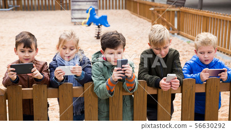 Children with phones near wooden fence 56630292