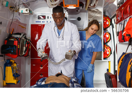 Emergency doctor resuscitating male patient with help of defibrillator Emergency doctor resuscitating male patient with help of defibrillator 56630706