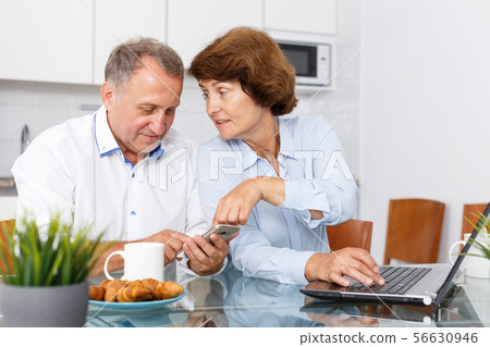 Mature man and woman using smartphone and working at laptop Mature man and woman using smartphone and working at laptop 56630946