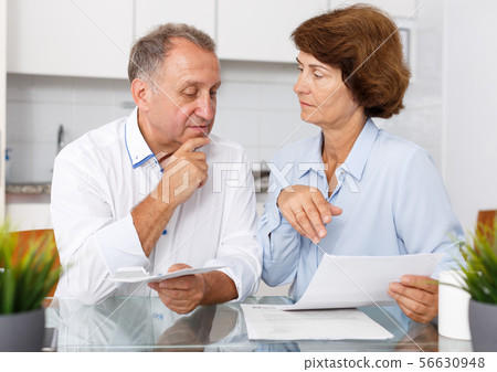 Sad mature couple at kitchen table sitting with financial documents Sad mature couple at kitchen table sitting with financial documents 56630948