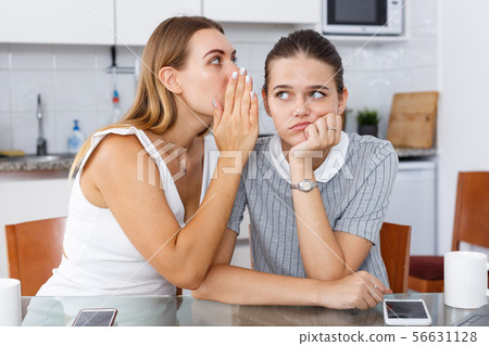 Sad young smiling girlfriends whispers in the ear and sharing secrets Sad young smiling girlfriends whispers in the ear and sharing secrets 56631128