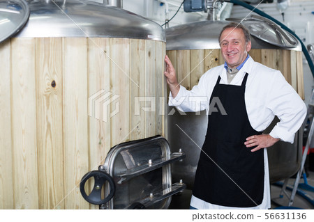 Brewer is standing near reservoir for beer on his workplace Brewer is standing near reservoir for beer on his workplace 56631136