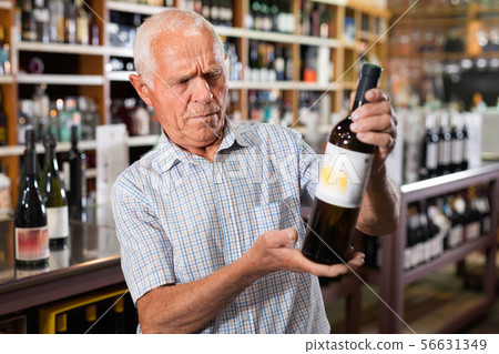 Positive grey-haired elderly man choosing wine in modern wineshop Positive grey-haired elderly man choosing wine in modern wineshop 56631349