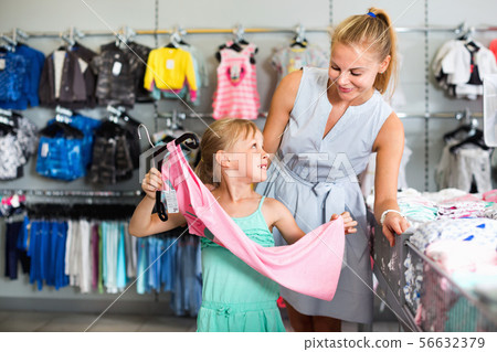 Female with girl choosing different clothes in the dress shop Female with girl choosing different clothes in the dress shop 56632379