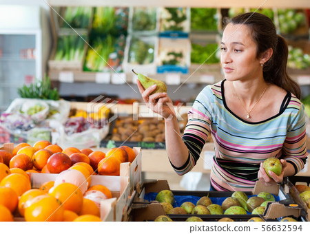 Positive Caucasian female choosing fresh fruits at shop Positive Caucasian female choosing fresh fruits at shop 56632594