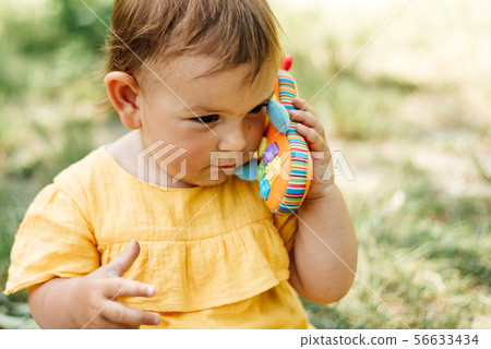 Curious little girl using toy phone outdoors in summer day. Gen z Curious little girl using toy phone outdoors in summer day. Gen z 56633434