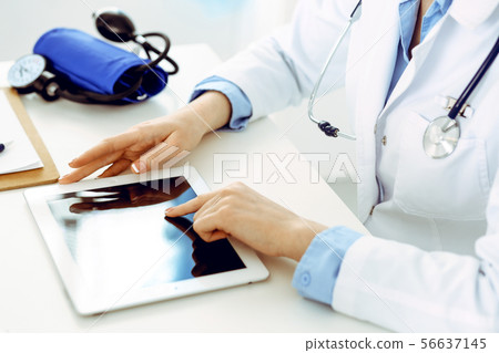 Doctor working table. Woman physician using tablet computer while sitting in hospital office close Doctor working table. Woman physician using tablet computer while sitting in hospital office close 56637145