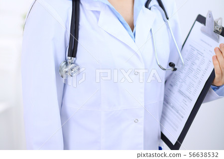 Stethoscope at female doctor breast at hospital office. Unknown physician's hands close-up. Medicine 56638532