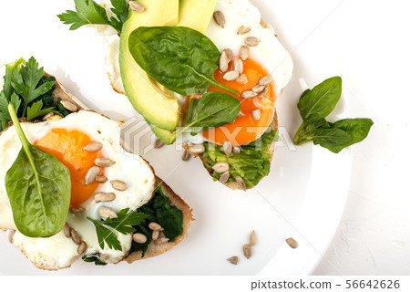 Fried eggs on a toasts bread with avocado, spinach and seeds on a white plate on the white 56642626