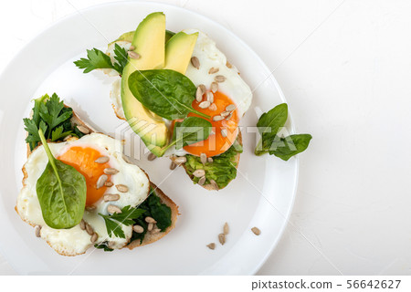 Fried eggs on a toasts bread with avocado, spinach and seeds on a white plate on the white Fried eggs on a toasts bread with avocado, spinach and seeds on a white plate on the white 56642627