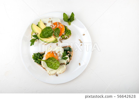 Fried eggs on a toasts bread with avocado, spinach and seeds on a white plate on the white Fried eggs on a toasts bread with avocado, spinach and seeds on a white plate on the white 56642628