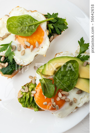 Breakfast on the white background. Fried eggs on a toasts bread with avocado, spinach and seeds on a 56642658