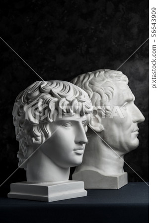 Gypsum copy of ancient statue Augustus and Antinous head on dark textured background. Plaster Gypsum copy of ancient statue Augustus and Antinous head on dark textured background. Plaster 56643909