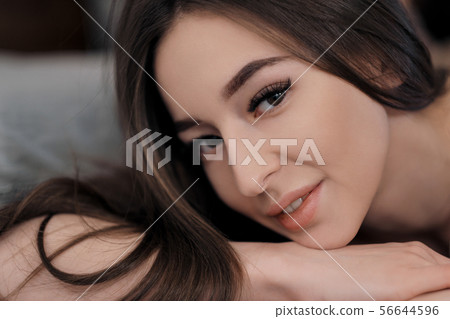 Beautiful brunette girl with brown eyes with bare shoulders lying on the bed. Face close up. Asian 56644596