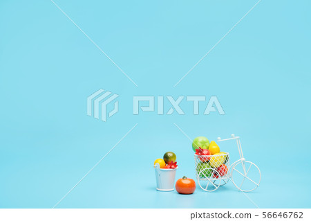 White wire bicycle with a basket filled with mini fruit. Near the bucket with vegetables and fruits White wire bicycle with a basket filled with mini fruit. Near the bucket with vegetables and fruits 56646762