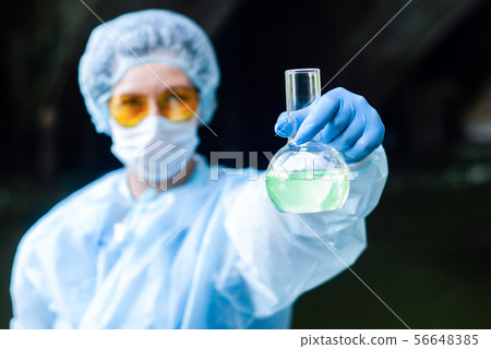 woman in medical or laboratory suit shows flask 56648385