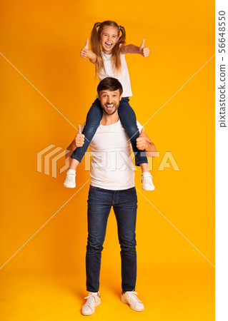 Joyful Father Carrying Daughter On Shoulders Gesturing Thumbs-Up, Studio Shot 56648550