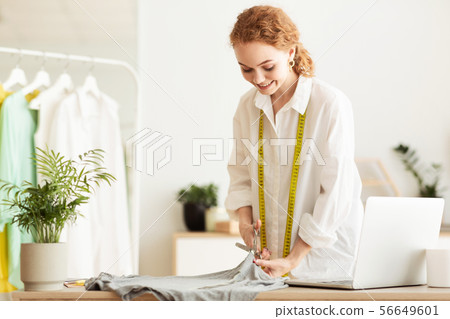 Young dressmaker cutting grey fabric in atelier Young dressmaker cutting grey fabric in atelier 56649601