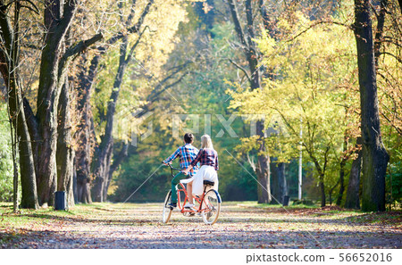 Young couple, handsome man and attractive woman on tandem bike in sunny summer park or forest. Young couple, handsome man and attractive woman on tandem bike in sunny summer park or forest. 56652016