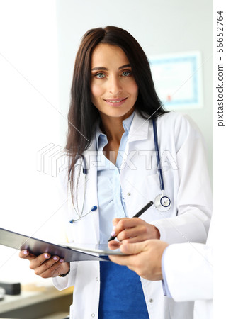 Smiling cheerful female GP making electronic notes Smiling cheerful female GP making electronic notes 56652764